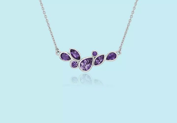 A February birthstone necklace of round, teardrop, and marquise amethyst, bezel-set in a cluster formation hanging from coordinating sterling silver chain